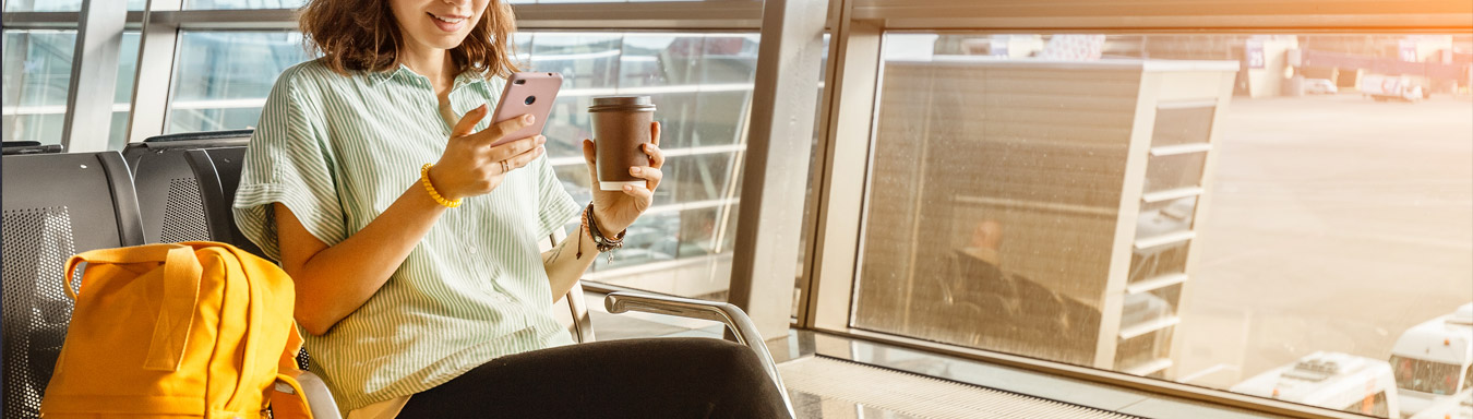 Dívka ve slaměném klobouku sedící na lavičce na letišti, surfující na internetu na mobilním telefonu